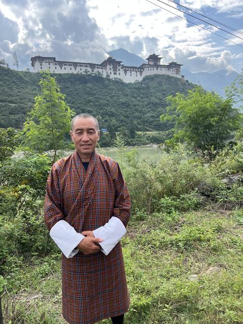 Man in traditional clothing posing with a temple in the background.