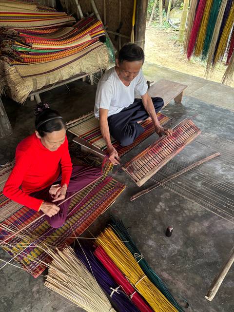       Two people weaving brightly colored textiles.
  