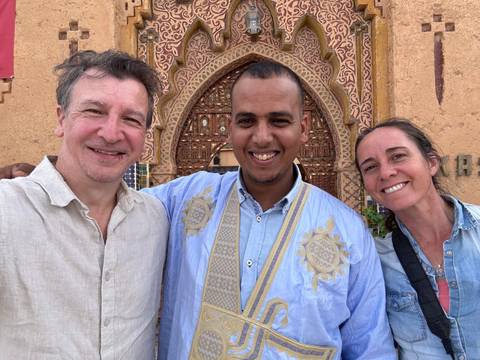       Three people smiling with intricate architecture in the background.
  