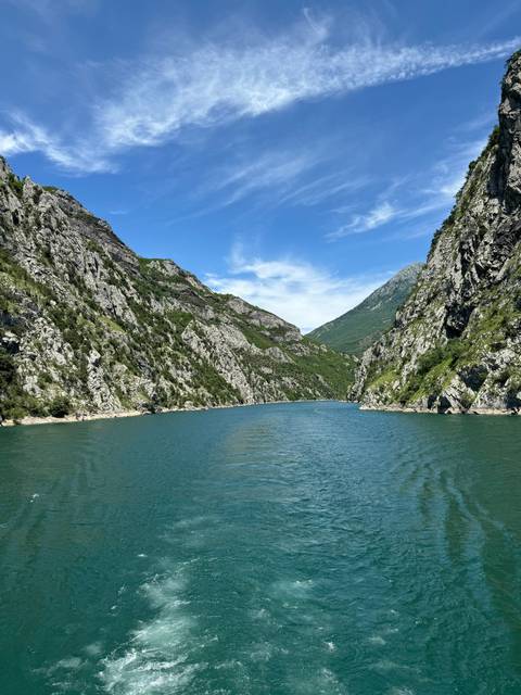 A wide river surrounded by tall mountains under a blue sky.