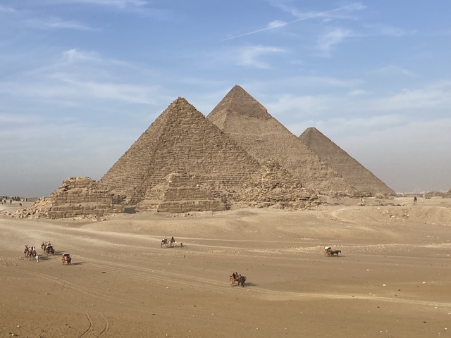       The Pyramids of Giza with blue skies and desert foreground.
  