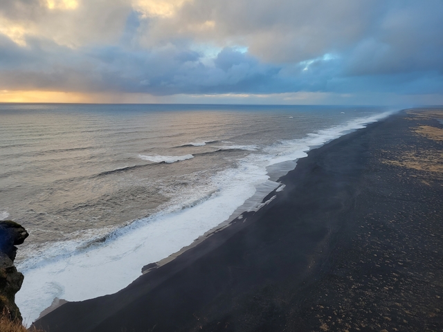 Black sand beach with waves and cloudy sky.