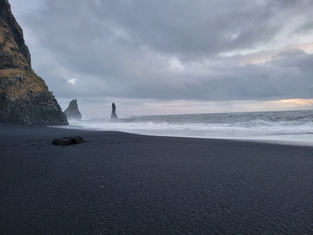 Black sand beach with rocky formations in the ocean.
