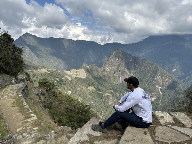       Person sitting on a cliff overlooking mountains.
  