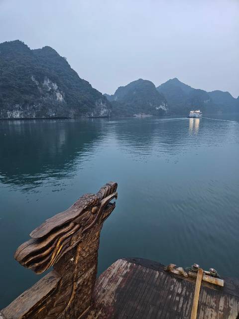       Decorative carved dragon head on a boat with a view of the bay.
  