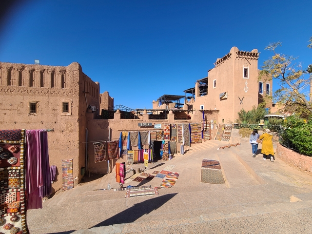 A street market with woven rugs and blue sky above.