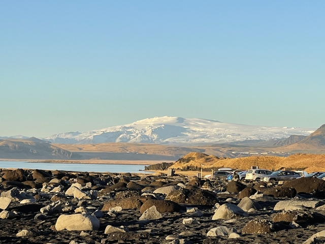       A distant glacier with rocky shore and vehicles.
  