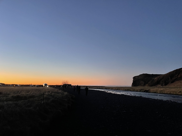 Riverbank at sunset with people walking.