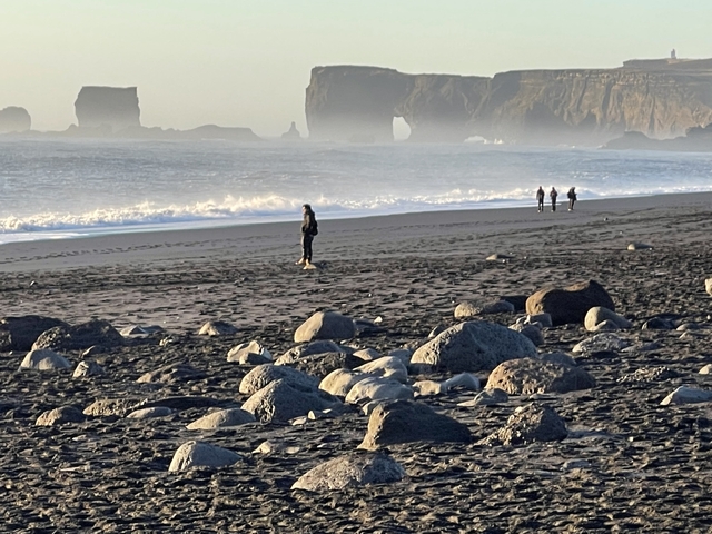 A person walking along a rocky beach with distant cliffs.