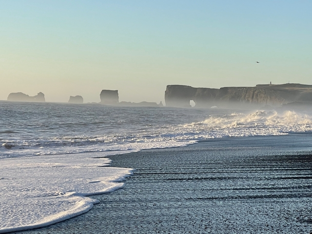 Waves crashing on a beach with sea stacks in the background.