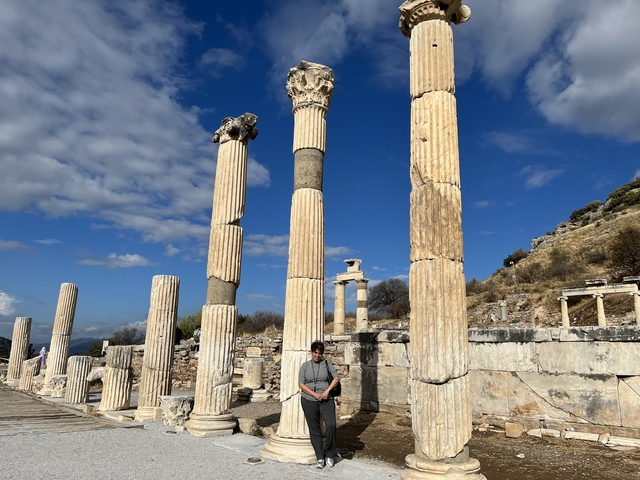 Person in front of ancient columns under a blue sky.
