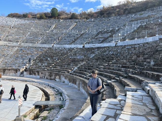 Tourist standing in ancient amphitheater ruins.