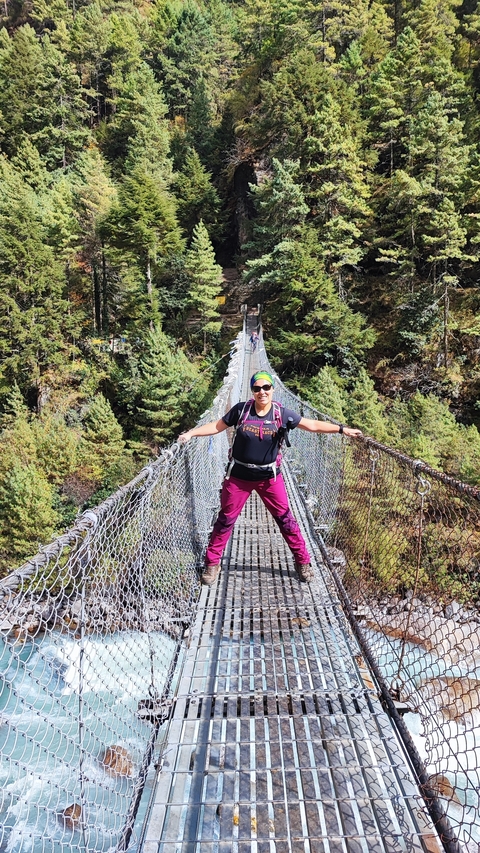 Hiker on a suspension bridge surrounded by forest.