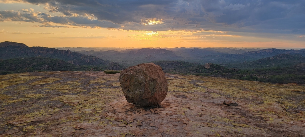 Sunset view over rocky terrain with a large boulder.
