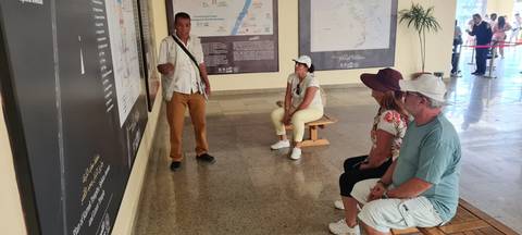       Guide showing maps and information to tourists indoors.
  