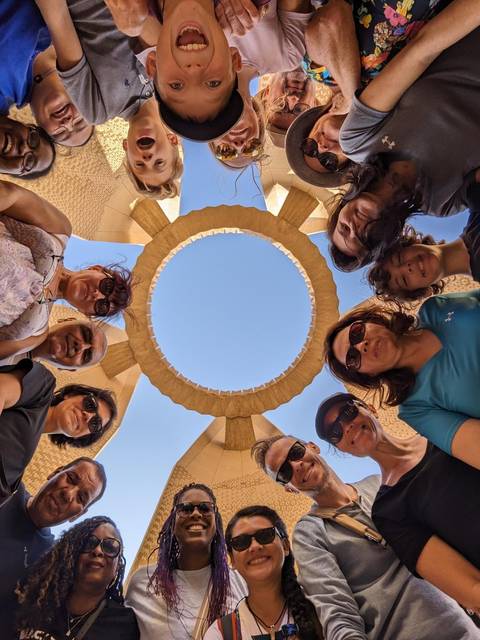       Group of people looking upwards in a circle with a sky view.
  