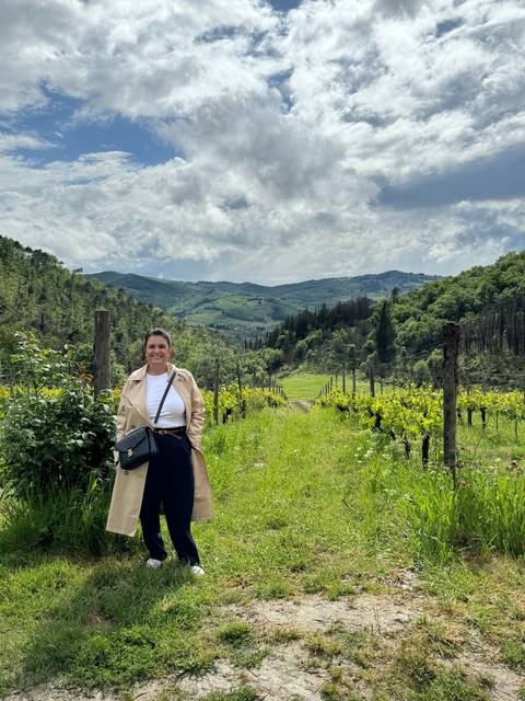       Woman posing in a vineyard with hills and cloudy sky in the background.
  
