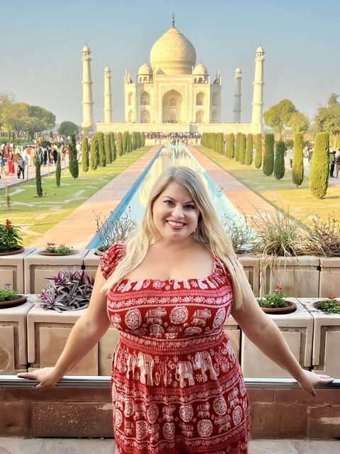 Smiling woman with long hair posing with a formal garden and pool in the background.