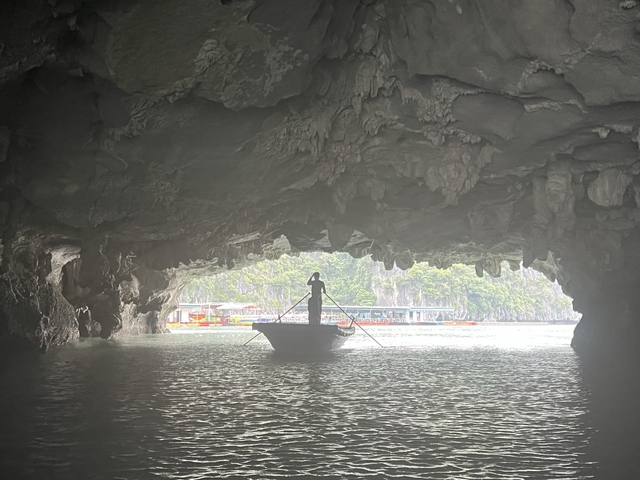       Person on a boat emerging from a cave with distant boats visible.
  