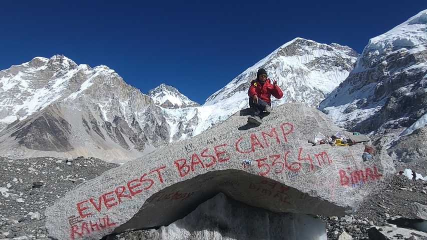 Person sitting on a rock with 'Everest Base Camp' inscription.