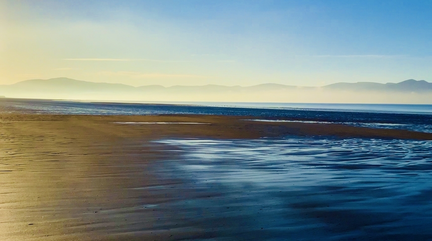       Peaceful beach landscape with mountains in the distance.
  