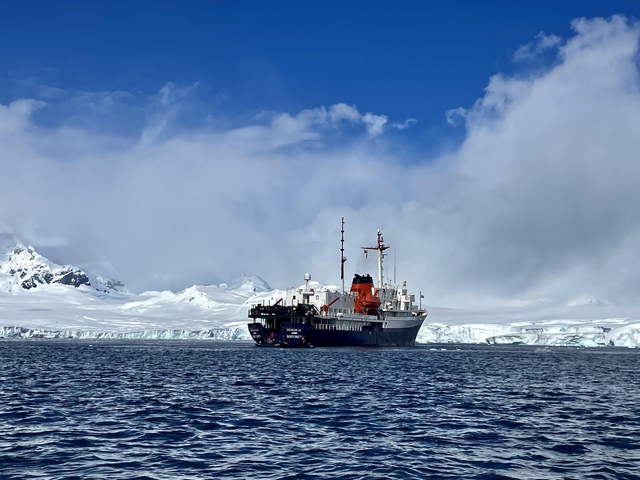 Ship navigating icy waters with snowy mountains in the background.