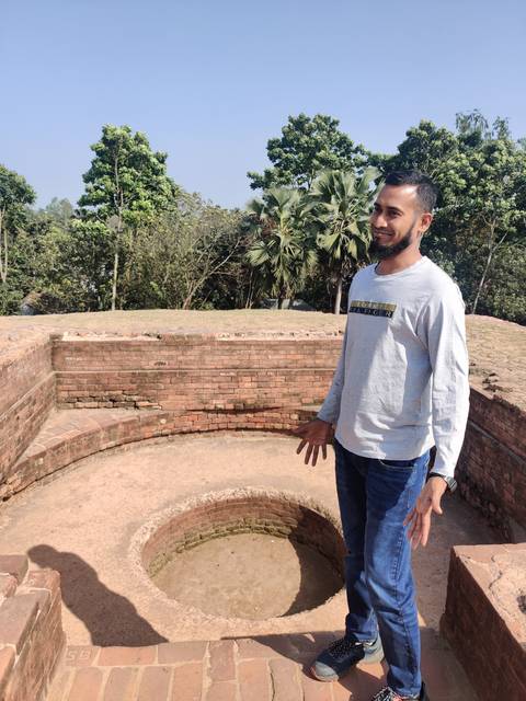       Man posing near ancient brick ruins with clear blue sky.
  
