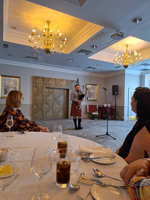 Person playing bagpipes inside a room with an audience.