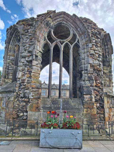       Stone ruins with flowers and a building in the background.
  