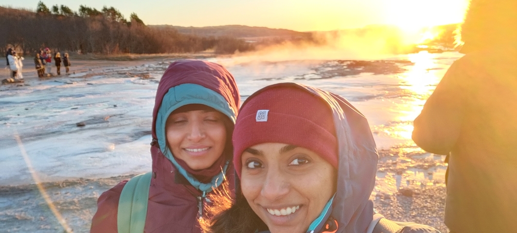       Two people near a geyser with sunset lighting
  