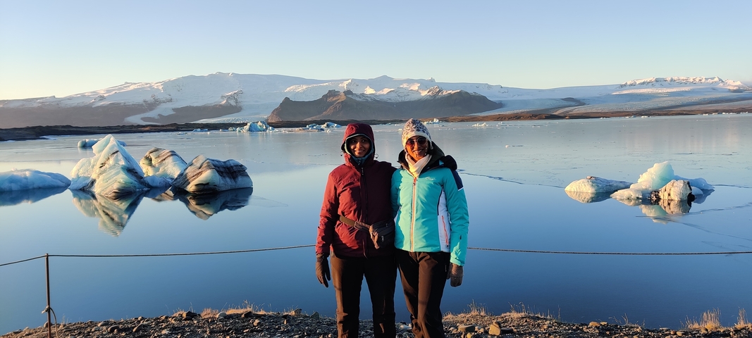       Couple standing by a glacial lagoon with floating icebergs
  