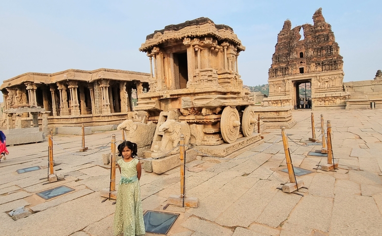       Girl posing in front of ancient stone chariots and temples.
  
