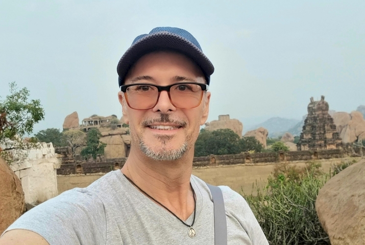       Man taking a selfie with rock formations and a historic structure in the background.
  