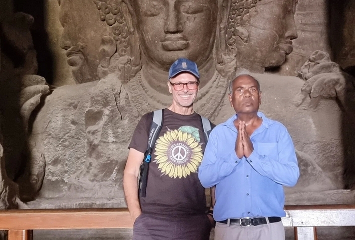       Two people standing in front of a carved rock relief.
  