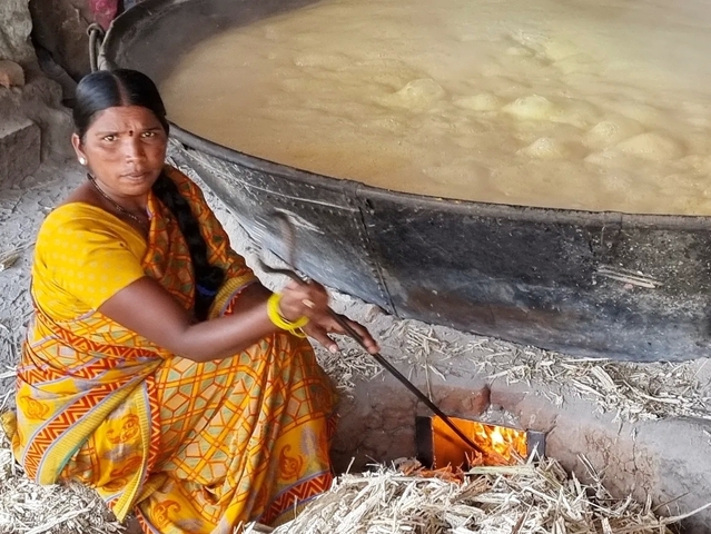       Woman cooking with a large pot over an open fire.
  