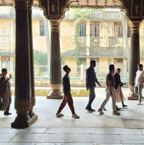       People walking indoors past large stone columns.
  