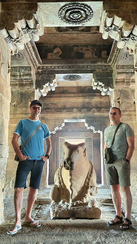       Two men posing with a Nandi statue inside a temple.
  