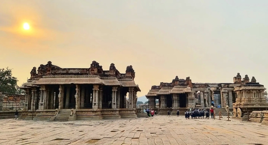       Ancient stone temple complex at sunset with people walking around.
  