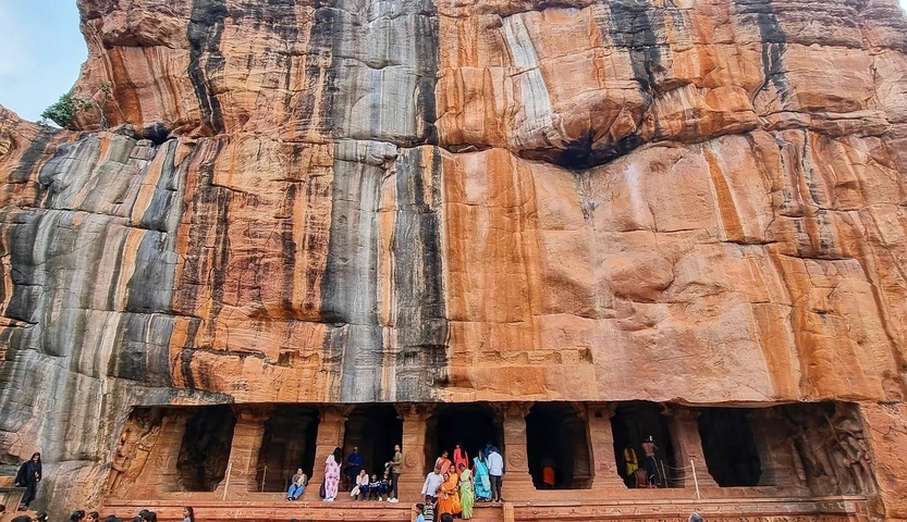       People standing in front of rock-cut caves.
  