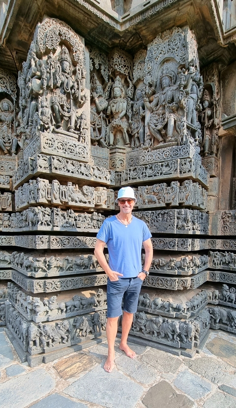       Man standing in front of intricately carved temple walls.
  