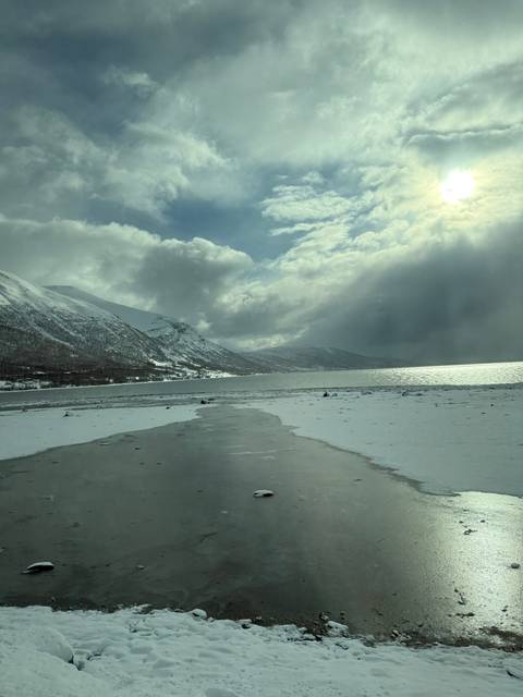       Frozen lake with mountains and a cloudy sky in the background.
  