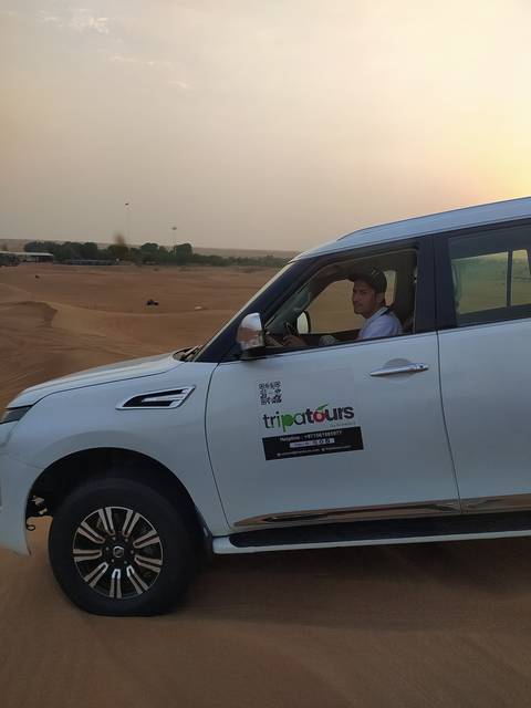       Vehicle driving through desert with a person visible through window.
  