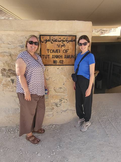       Two women standing next to a sign for Tutankhamun's tomb.
  
