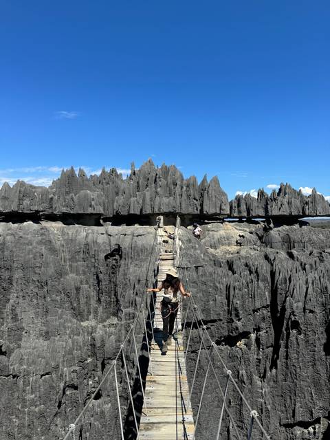       People crossing a suspension bridge over limestone formations.
  
