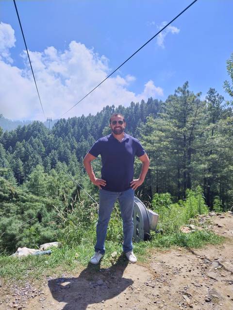       Individual posing among tall trees under a blue sky.
  