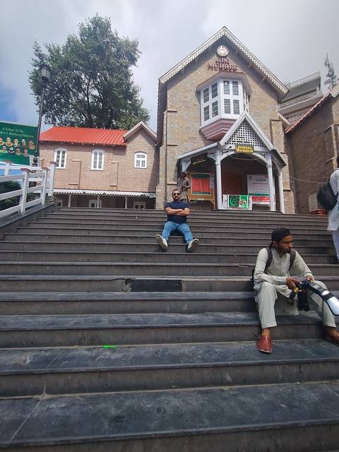       Person sitting on steps near a stone building.
  
