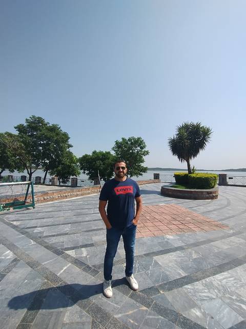       Person standing on a paved terrace with trees.
  