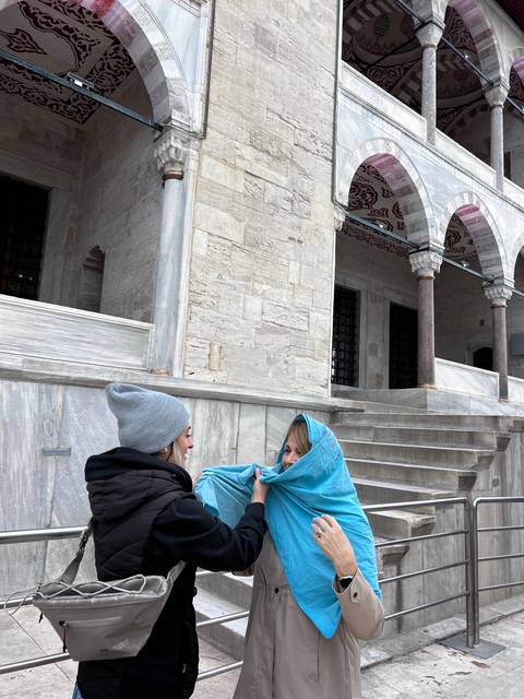       Two women wearing jackets near an ancient stone building.
  