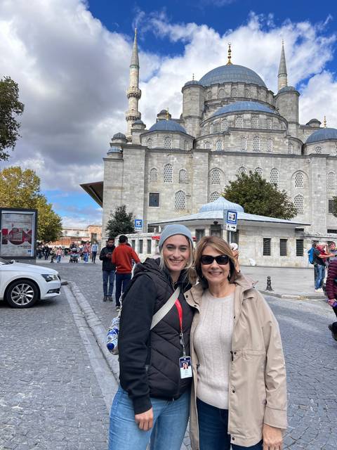       Two women posing in front of a mosque with a blue sky background.
  