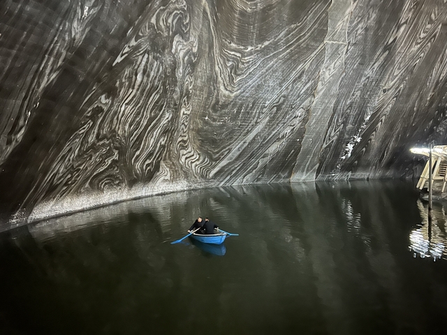 Two people in a rowboat inside a vast cave.